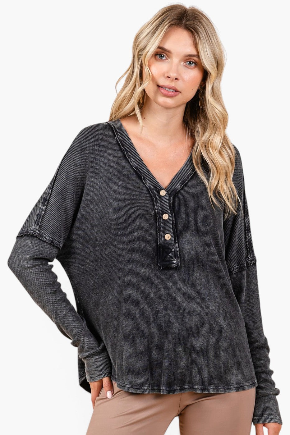 A woman modeling a dark gray washed long-sleeve henley top with a button placket, paired with tan pants, against a plain white background.