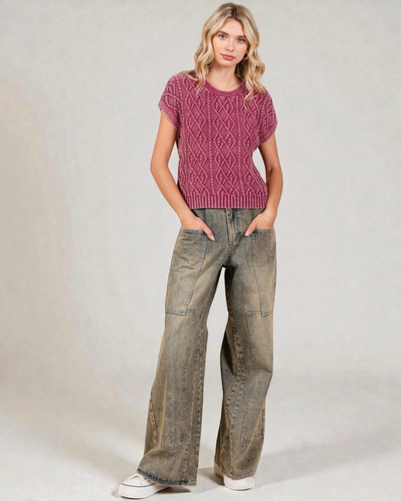 Woman wearing a pink knitted sweater and wide-leg jeans on a plain background