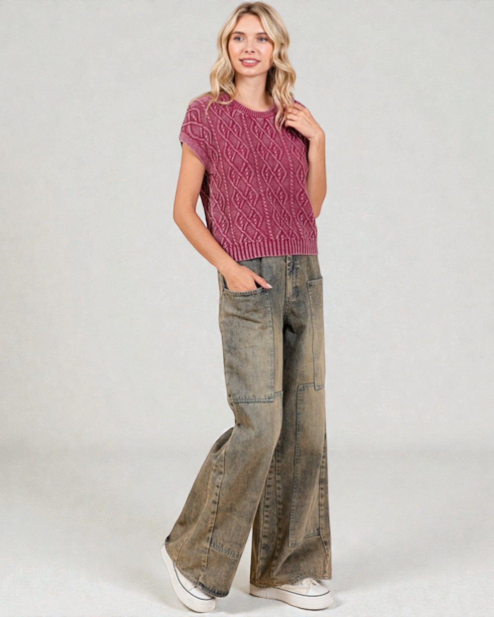 Woman wearing a pink knitted top and wide-leg jeans on a white background