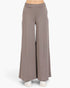 A pair of wide-leg, high-waisted pants in a muted taupe-brown color, shown on a model from the waist down wearing white sneakers against a plain white background.