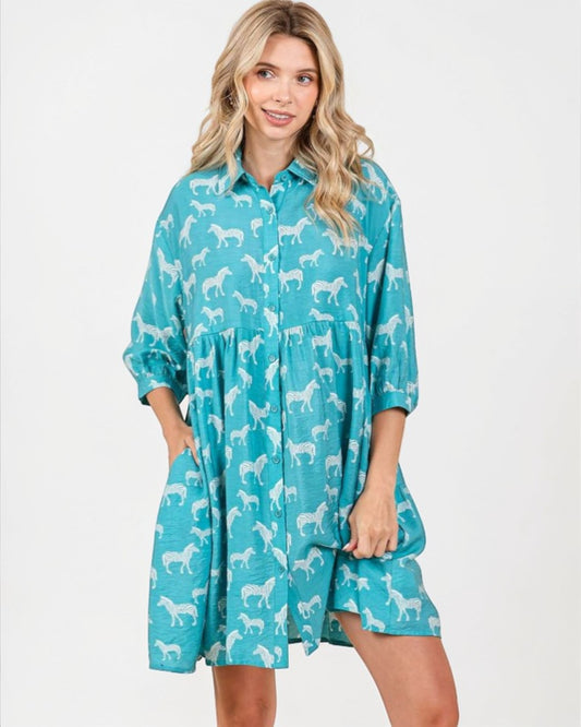 Woman wearing a teal dress with white horse pattern on a white background