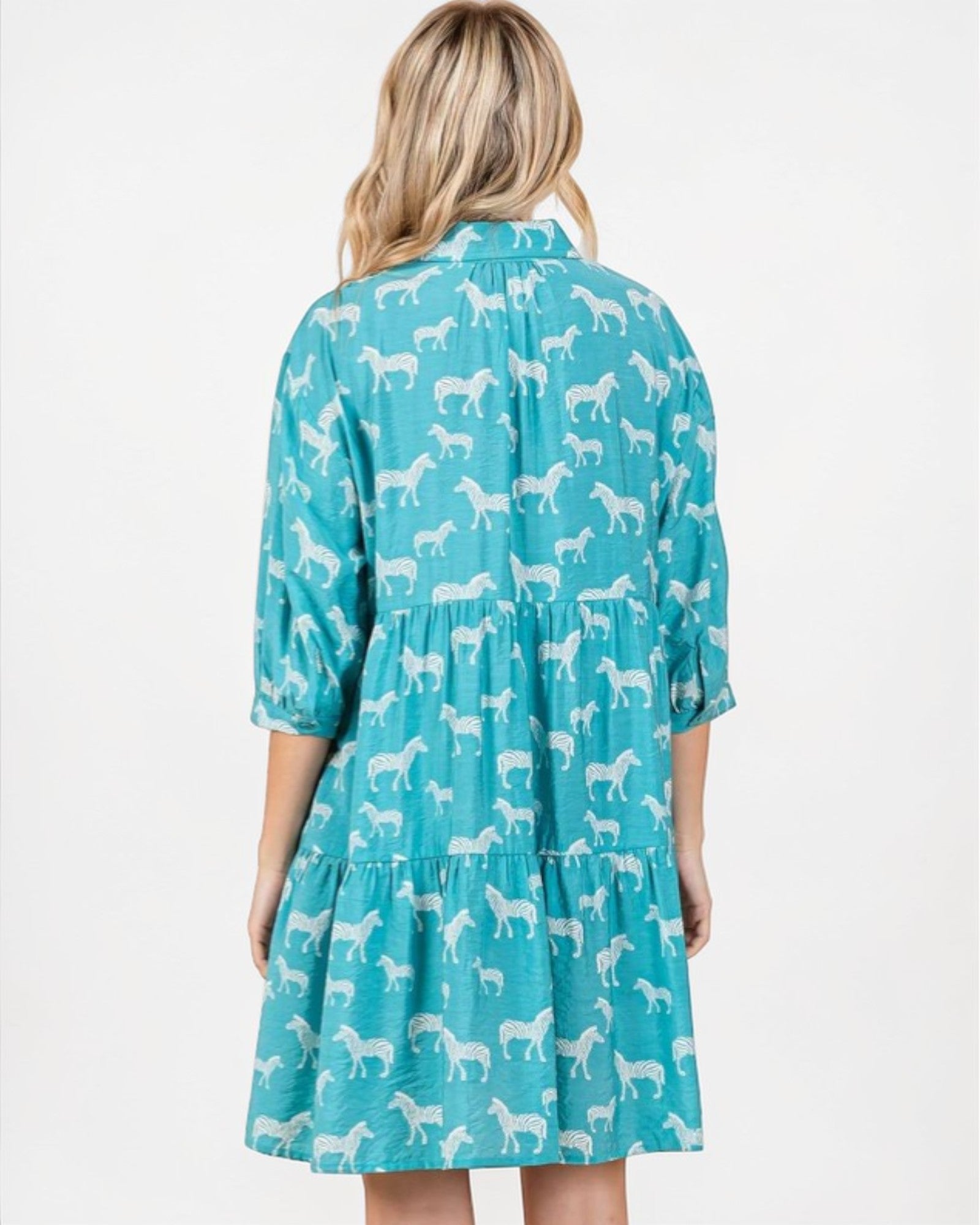 Woman wearing a teal dress with white horse pattern on a white background