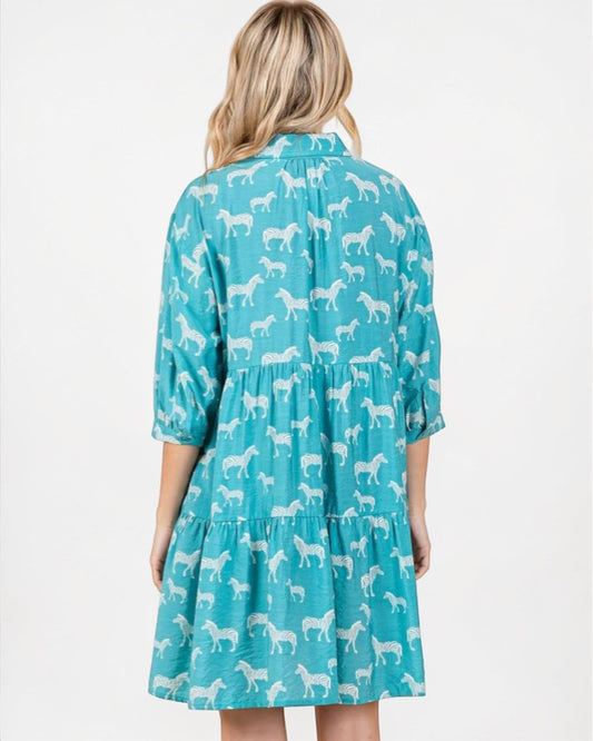Woman wearing a teal dress with white horse pattern on a white background