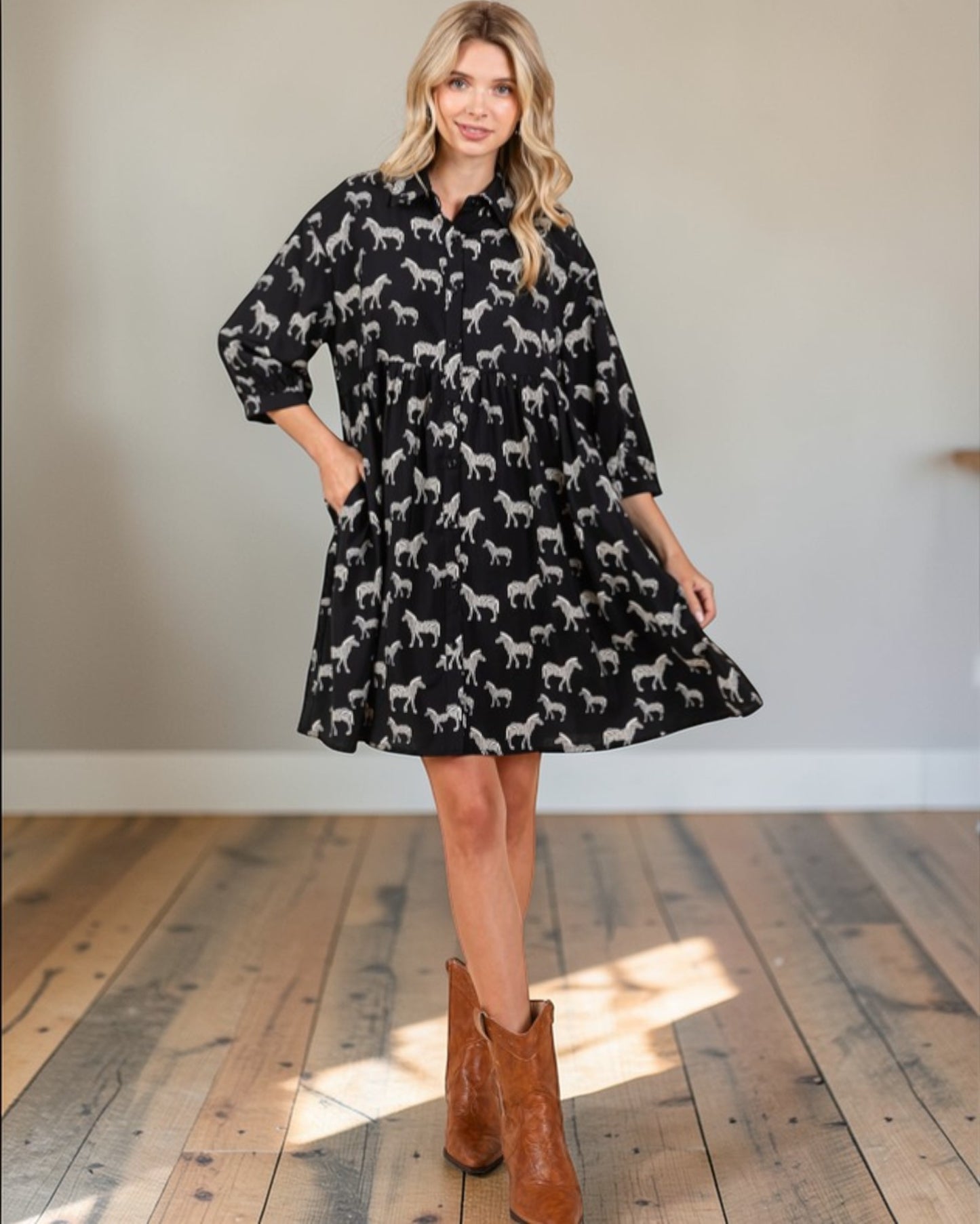 Woman wearing a black dress with white zebra pattern and brown boots indoors.