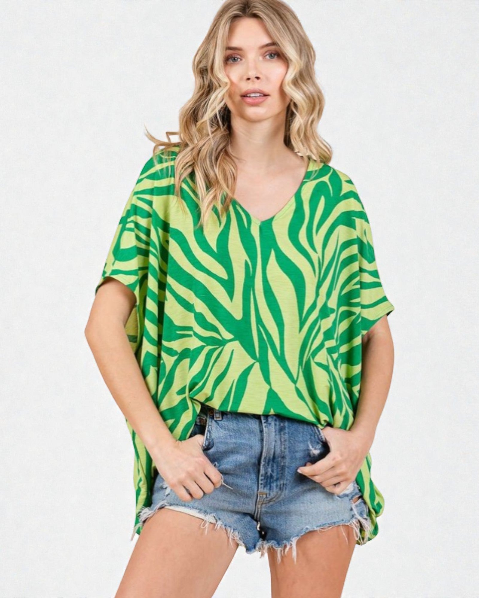 Woman wearing a green and white patterned top with denim shorts on a white background