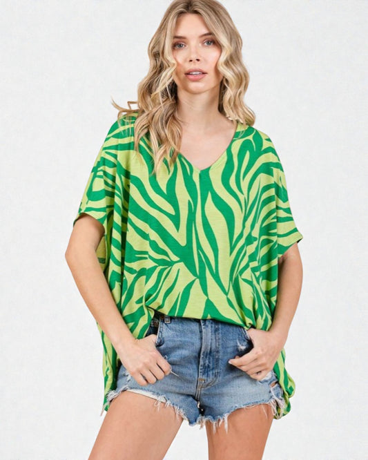 Woman wearing a green and white patterned top with denim shorts on a white background
