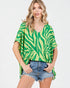 Woman wearing a green and white patterned top with denim shorts on a white background
