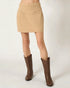 Beige skirt worn with brown cowboy boots on a white background