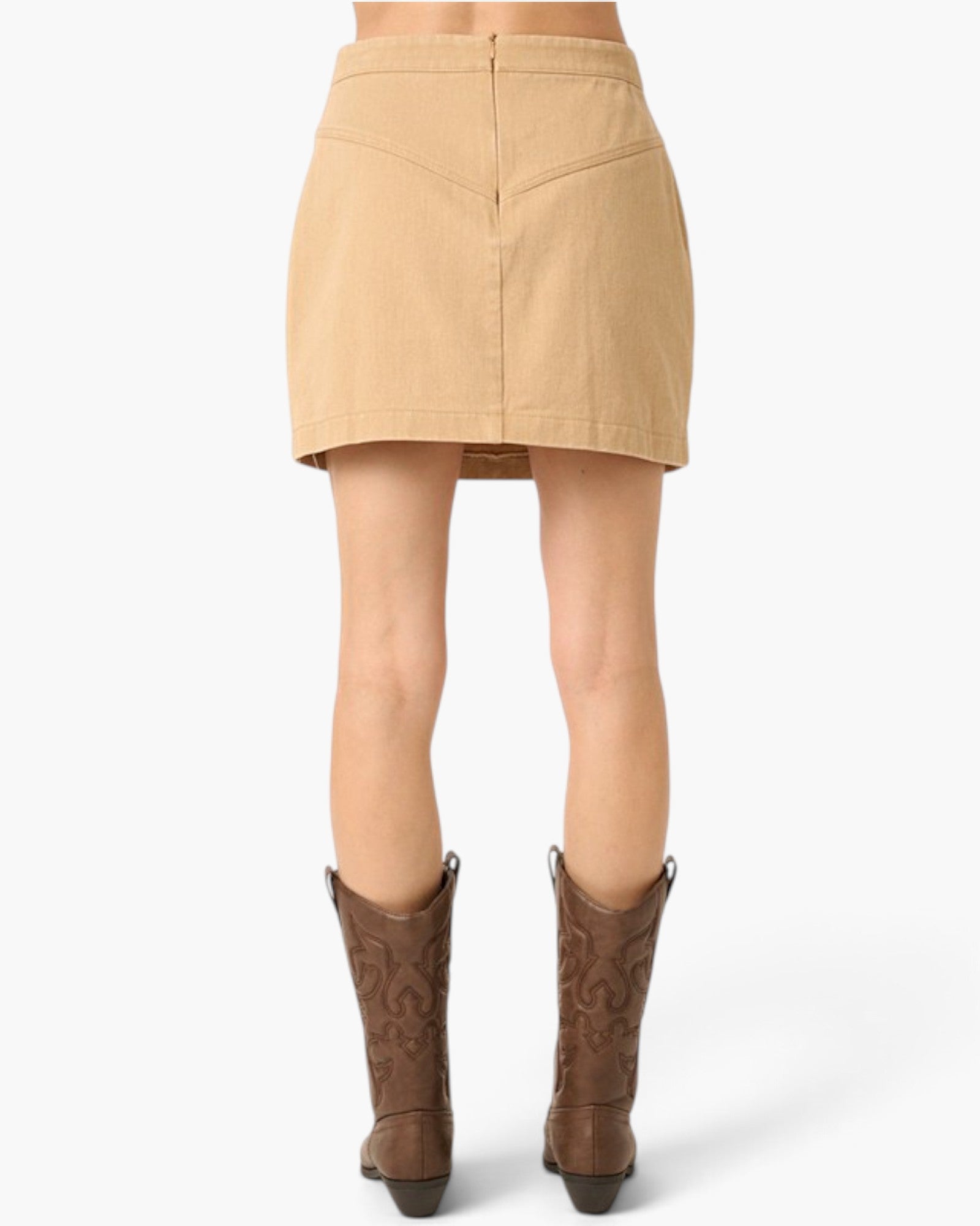 A tan mini skirt shown from the back on a model, paired with brown cowboy boots against a light gray studio background.
