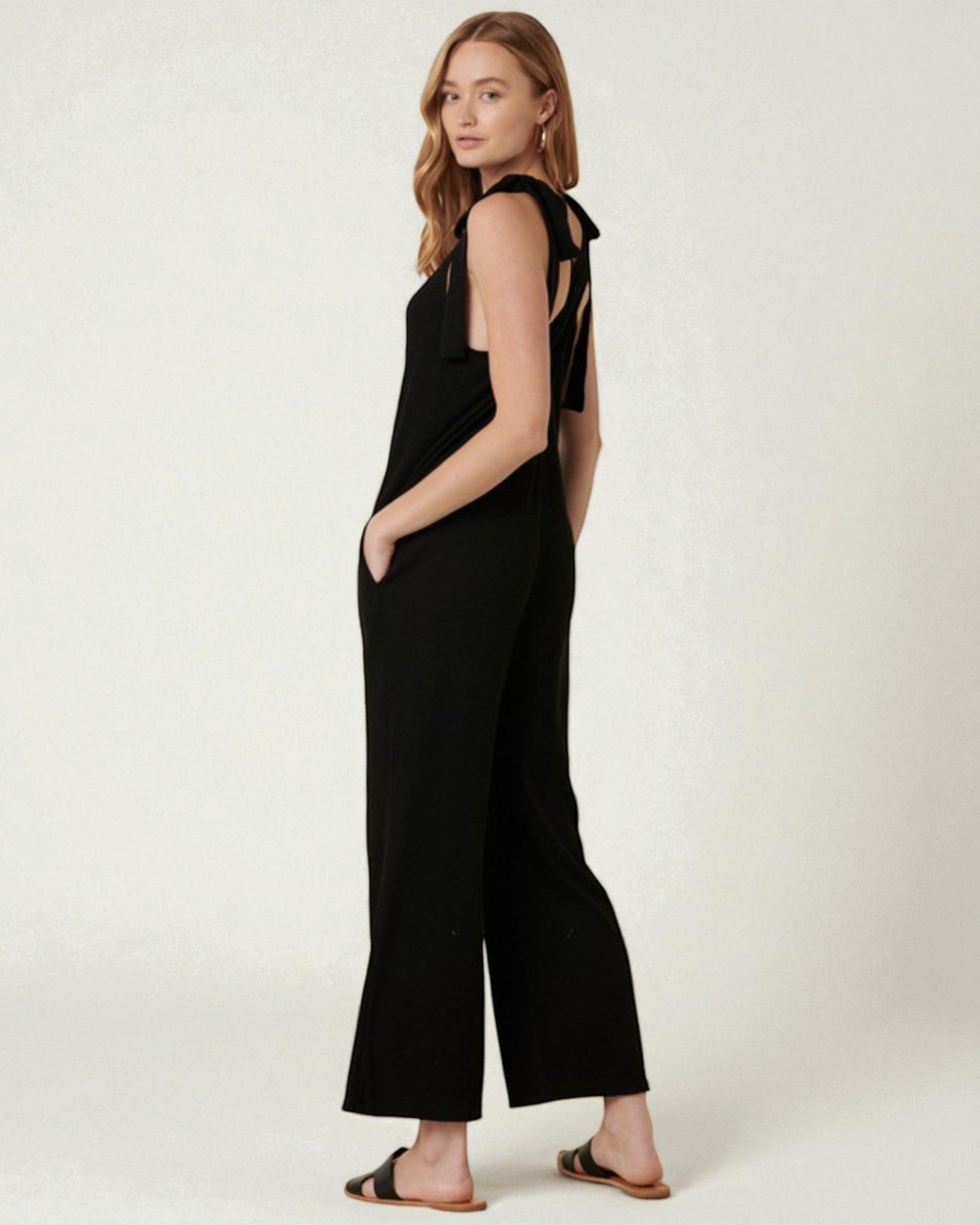 Woman wearing a black jumpsuit with cut-out shoulders on a white background