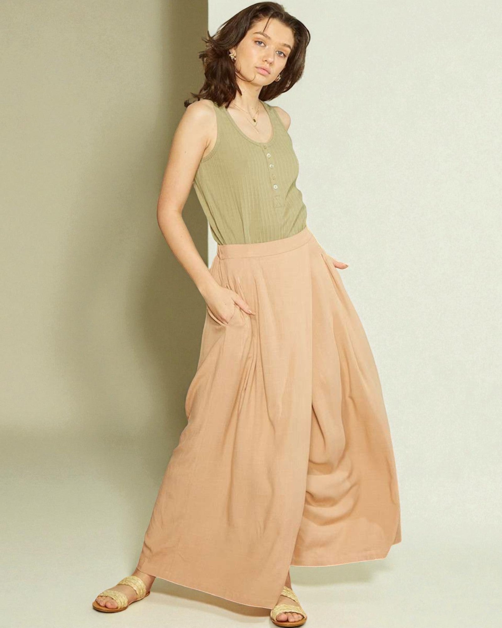Woman wearing a green sleeveless top and beige flowing pants against a plain background