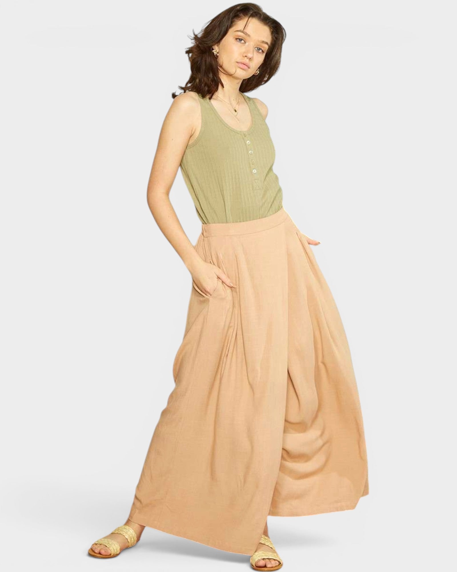 Woman wearing a green sleeveless top and beige dhoti pants on a white background