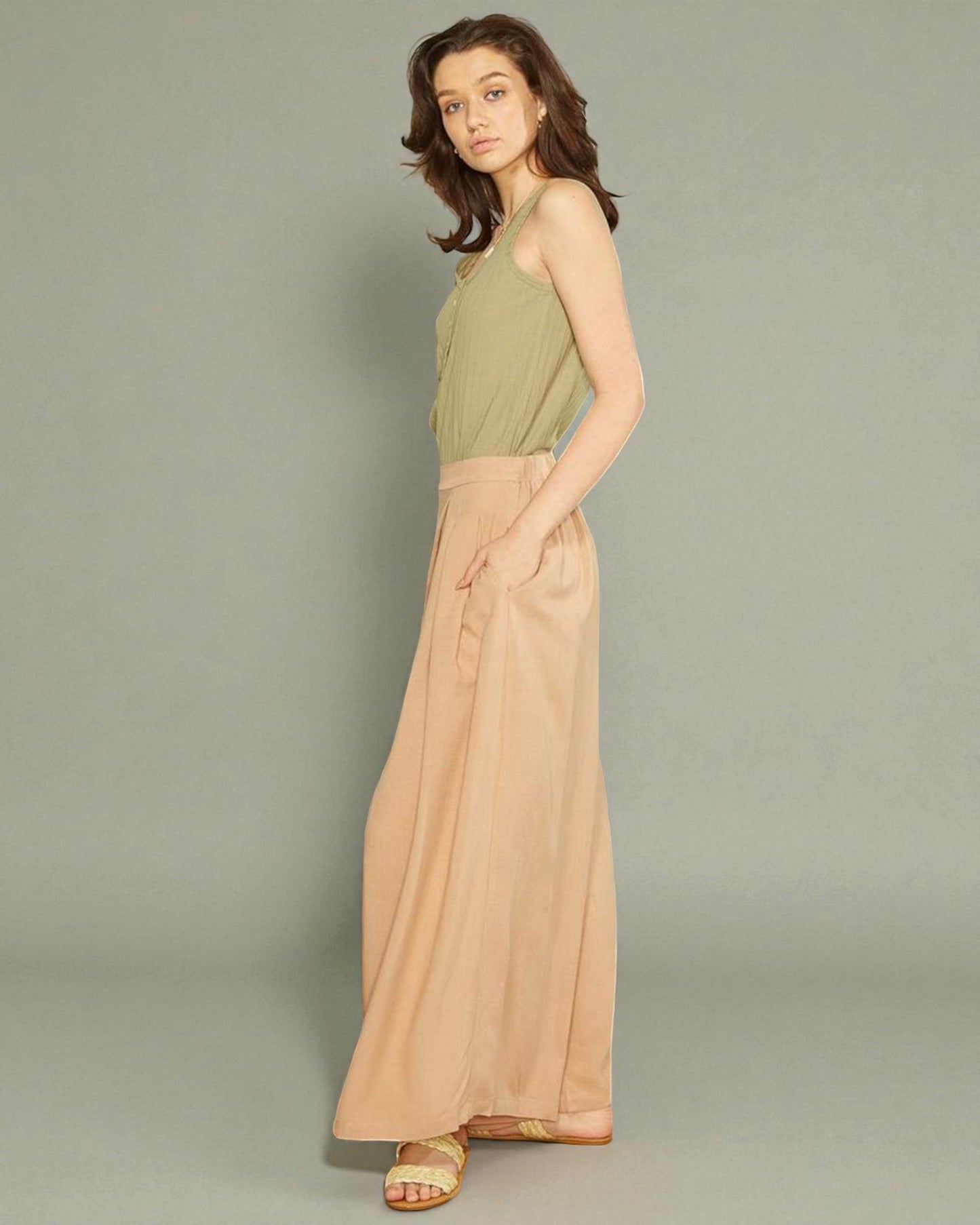 Woman wearing a green top and beige wide-leg pants on a gray background