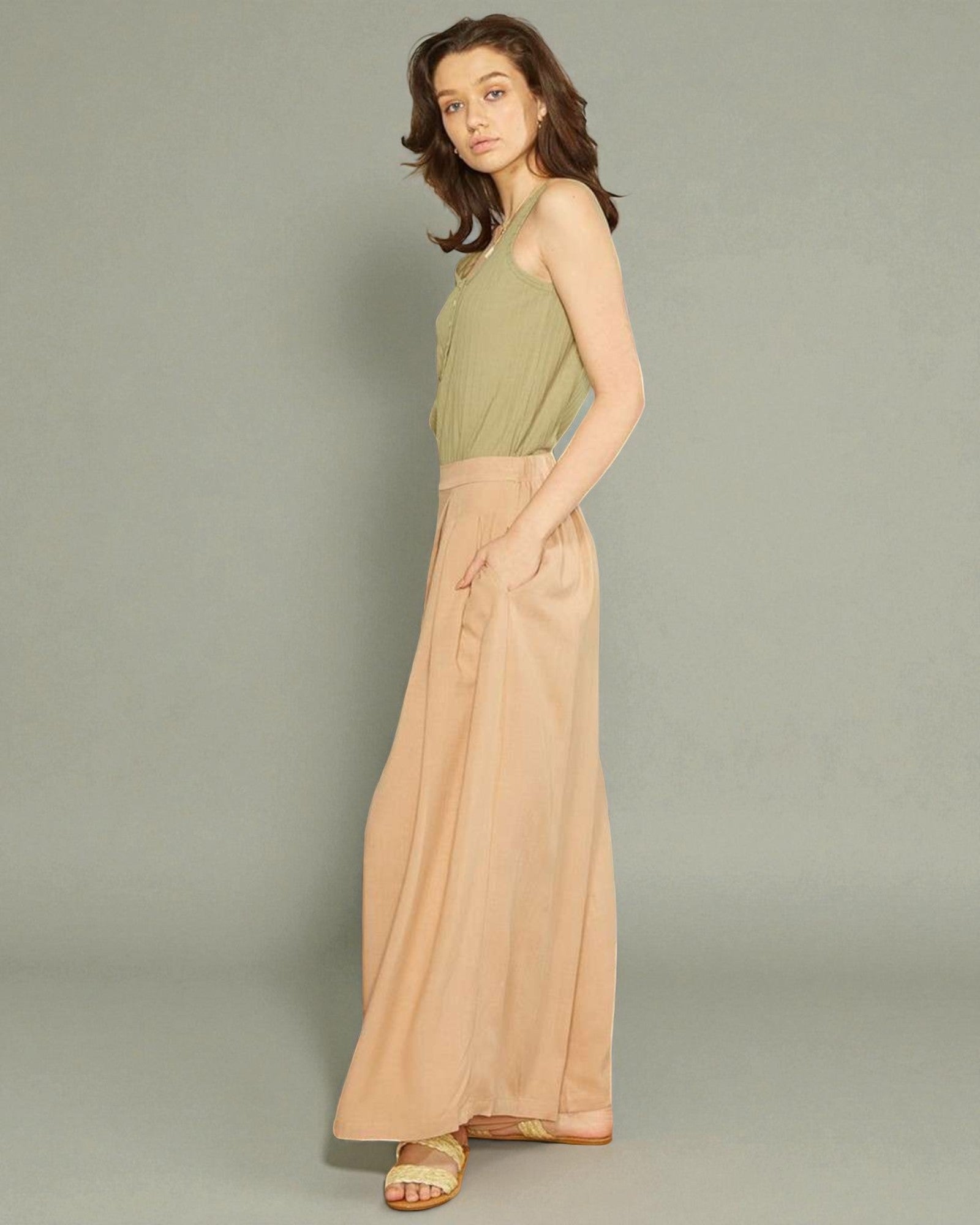 Woman wearing a green top and beige wide-leg pants on a gray background