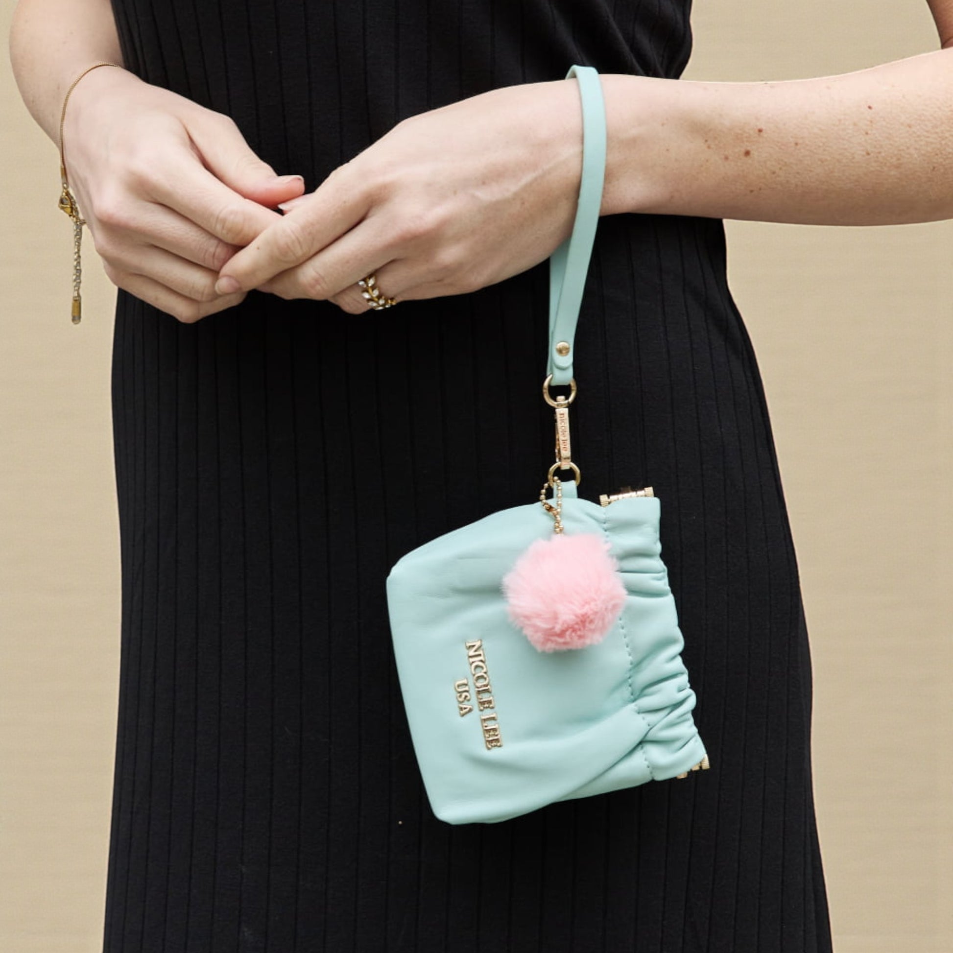 Light blue pouch with pink pom-pom and gold chain on a beige background
