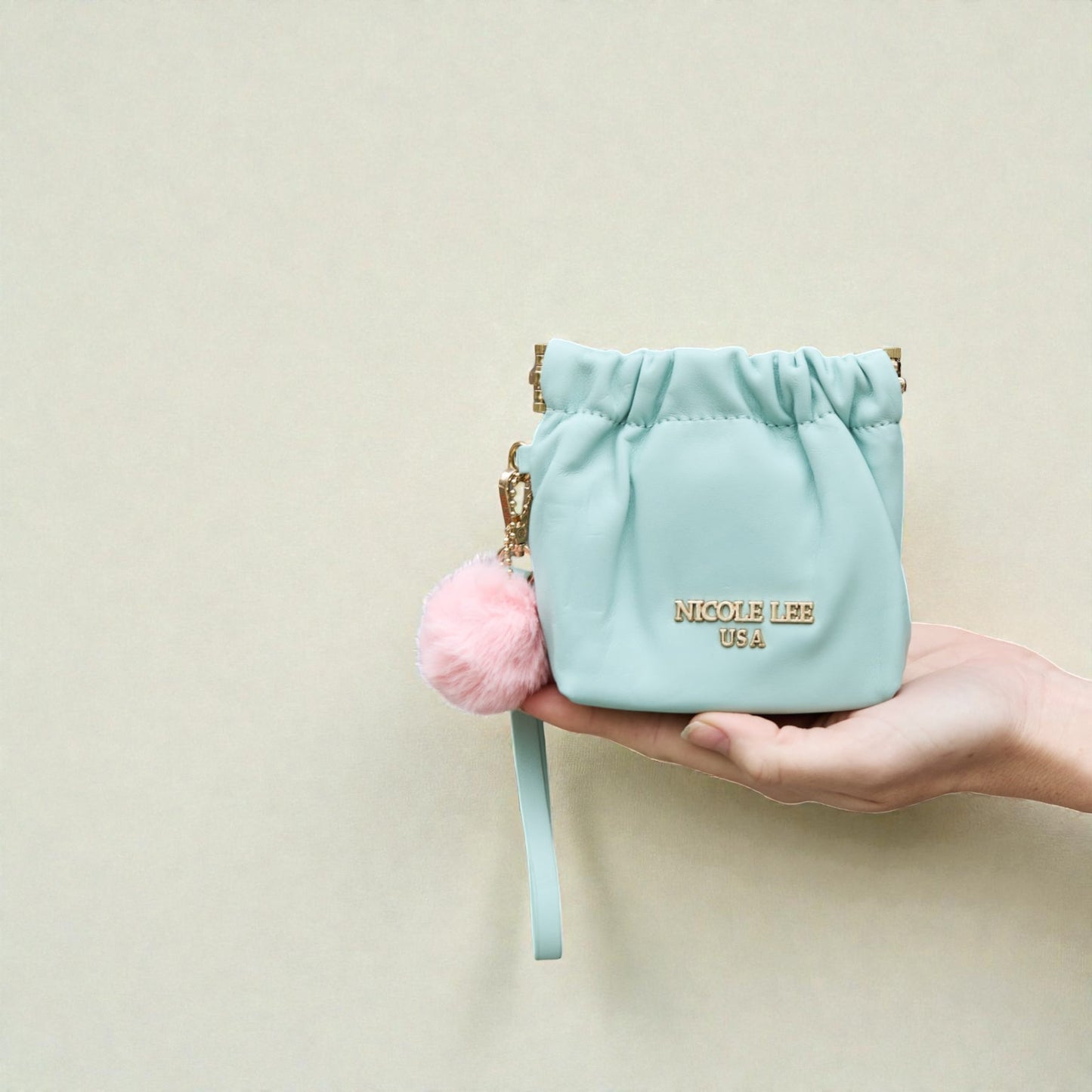 Light blue pouch with pink pom-pom and visible brand name on a beige background