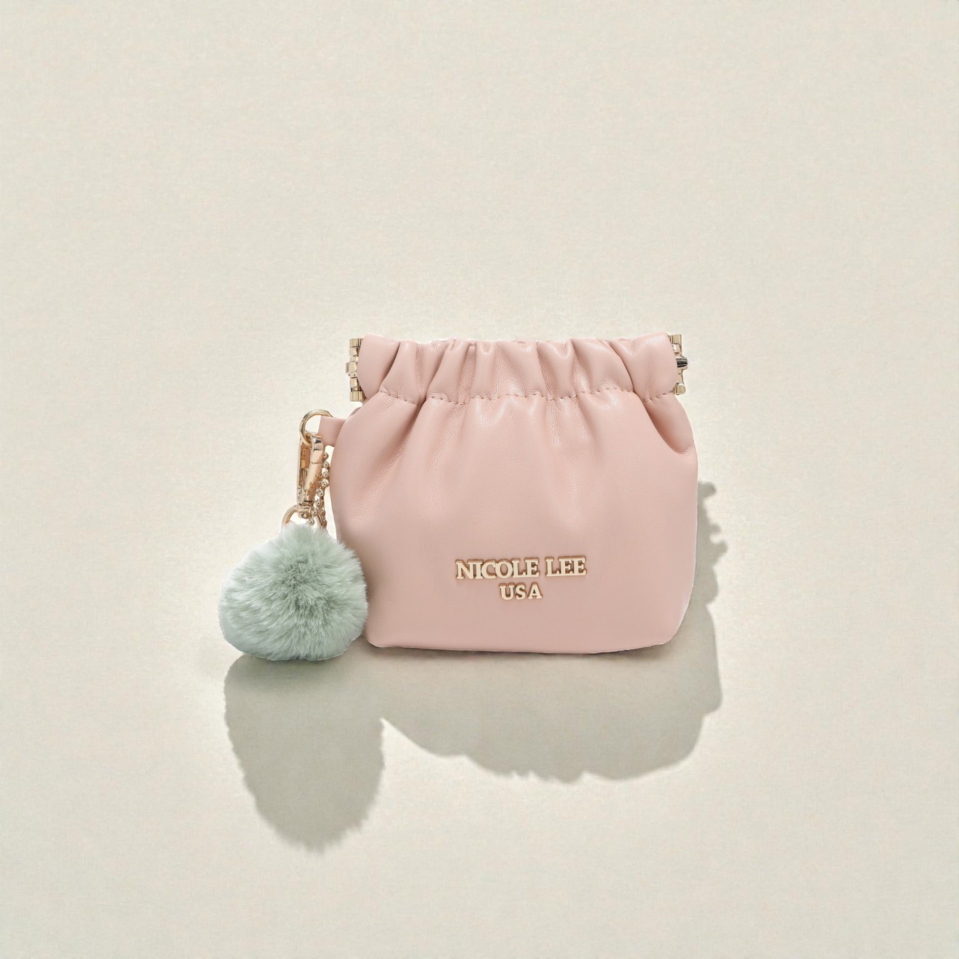 Pink pouch with a green pom-pom keychain on a beige background