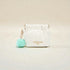 White pouch with a turquoise pom-pom on a beige background
