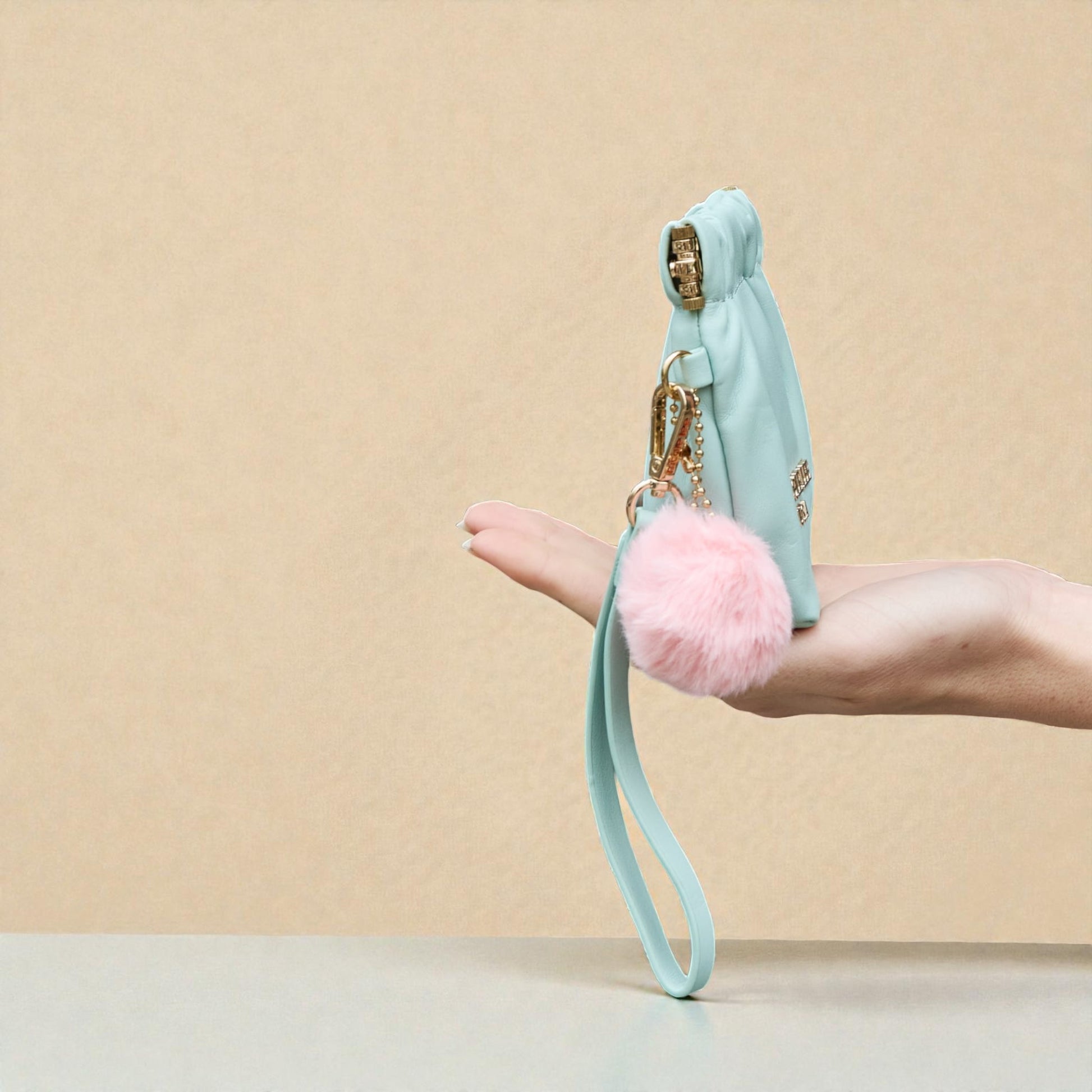 Light blue keychain with pink pom-pom held by a hand against a beige background
