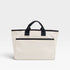 Beige tote bag with black handles and trim on a light gray background