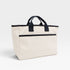 Beige tote bag with black handles and trim on a light gray background