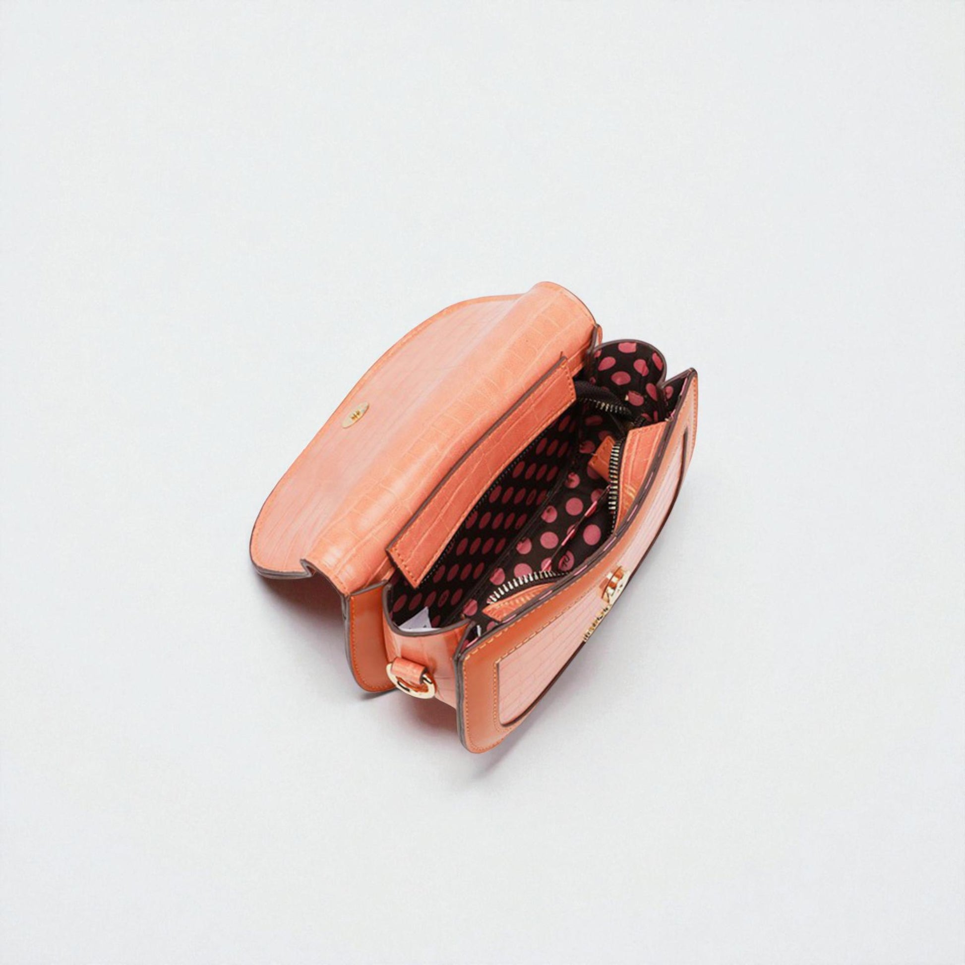 Open peach-colored handbag with polka dot interior on a light gray background