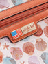 Close-up of a brown leather product with 'nicole lee' label on a shell-patterned background