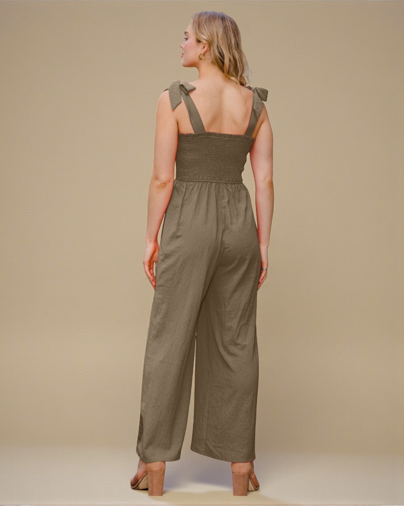 Woman wearing an olive green jumpsuit with a plain background