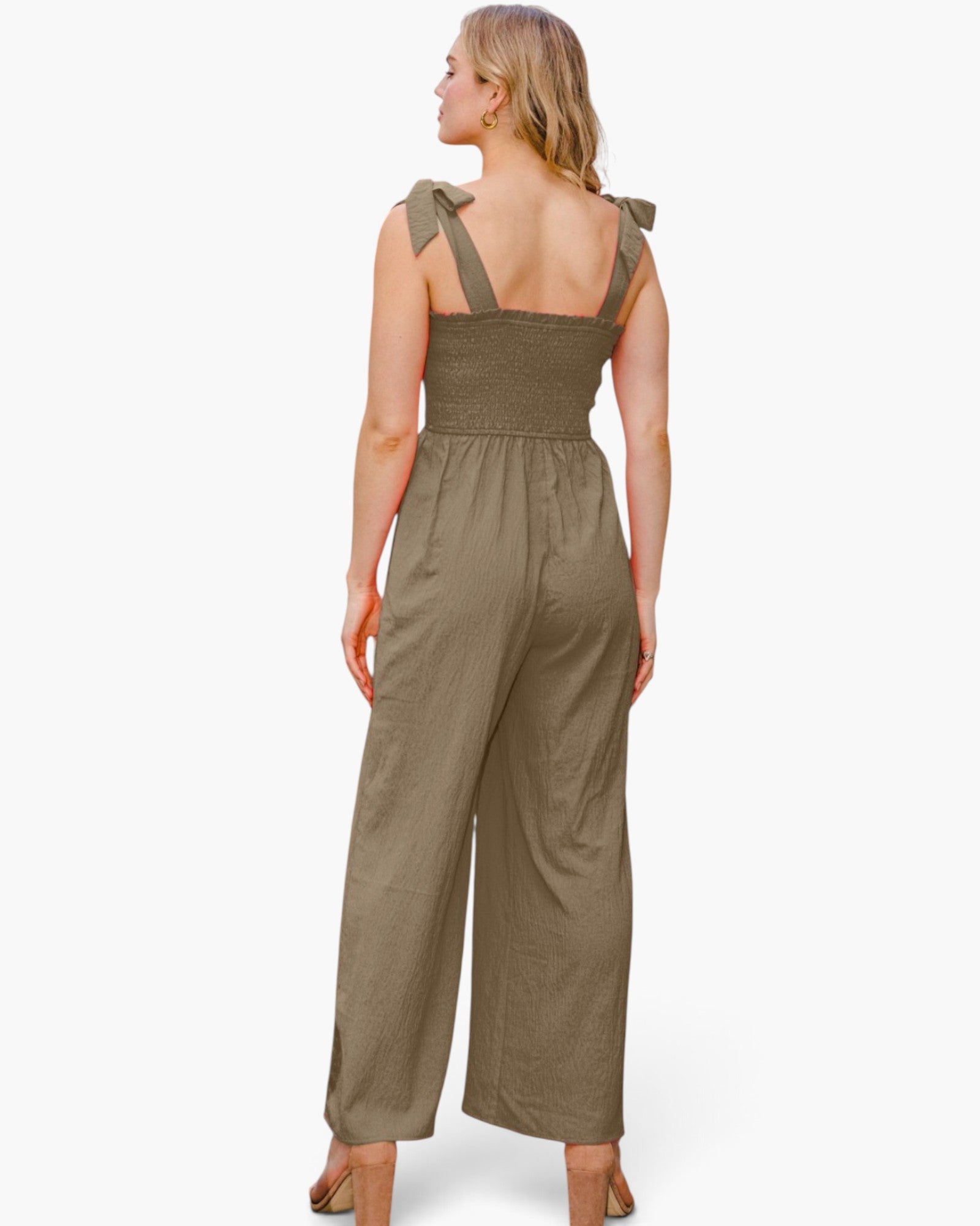 A woman shown from the back wearing an olive green wide-leg jumpsuit with shoulder tie details and a smocked bodice, photographed against a clean white studio background.