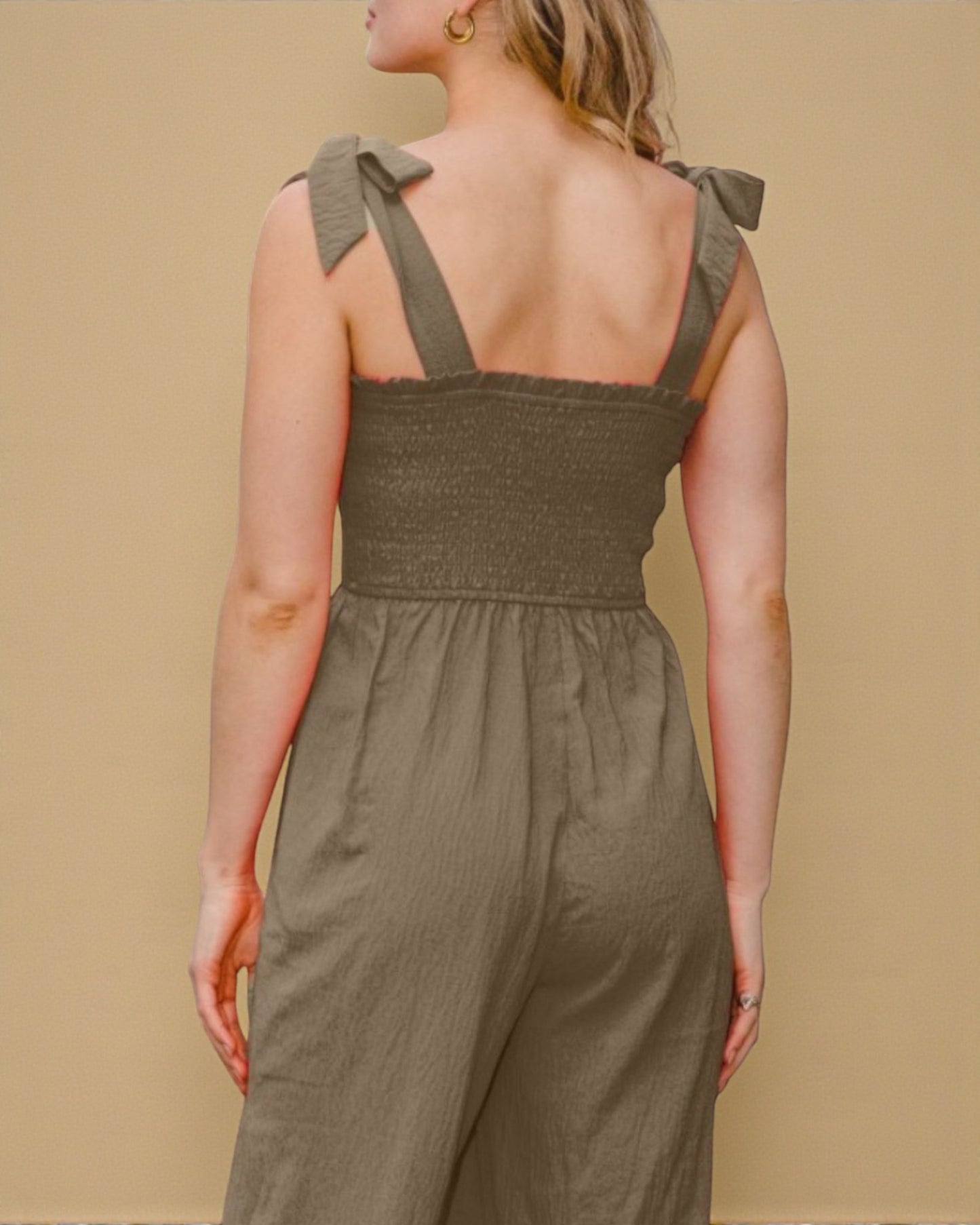Person wearing a green jumpsuit with bow straps on a beige background