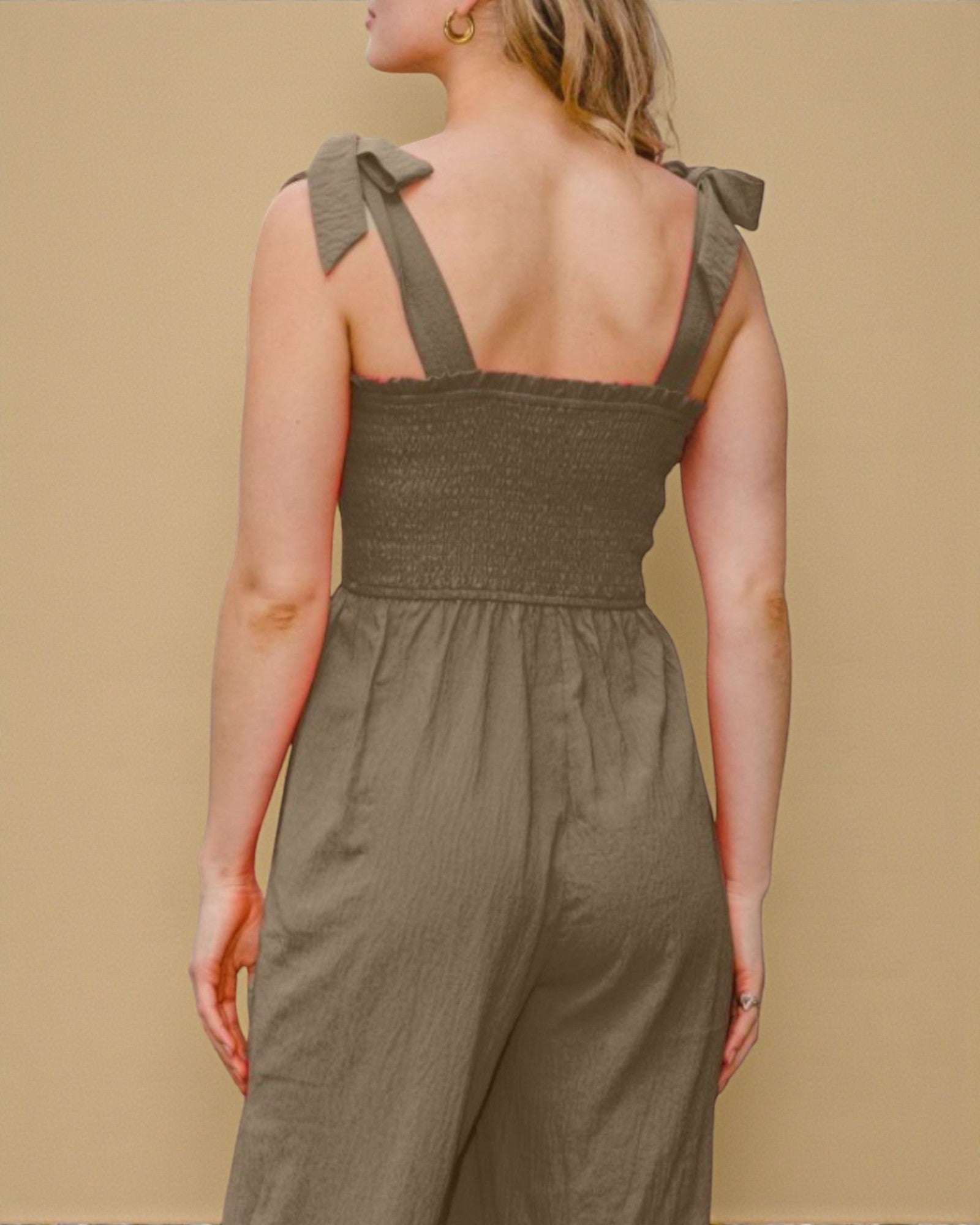 Person wearing a green jumpsuit with bow straps on a beige background