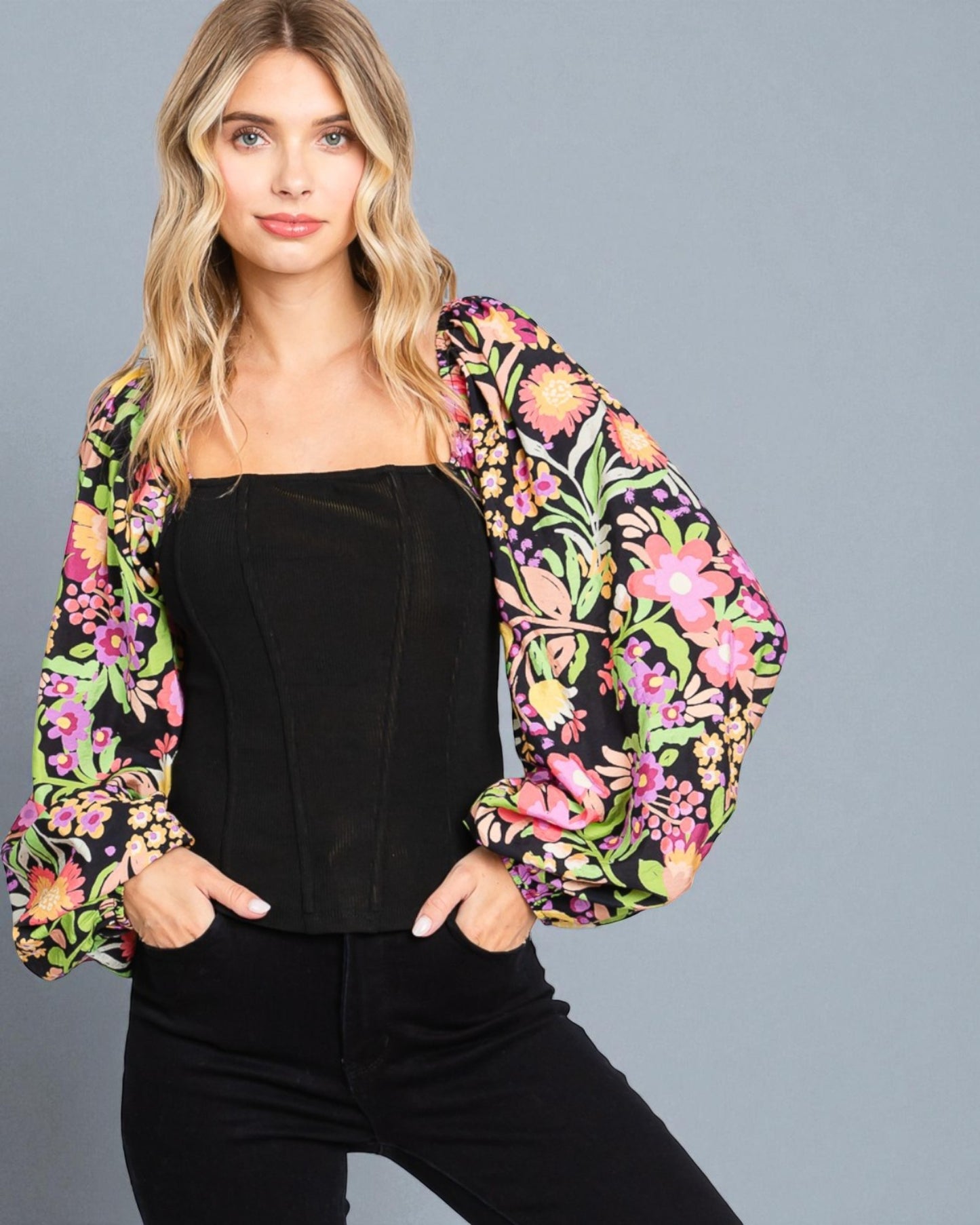 Woman wearing a black top and colorful floral jacket against a gray background