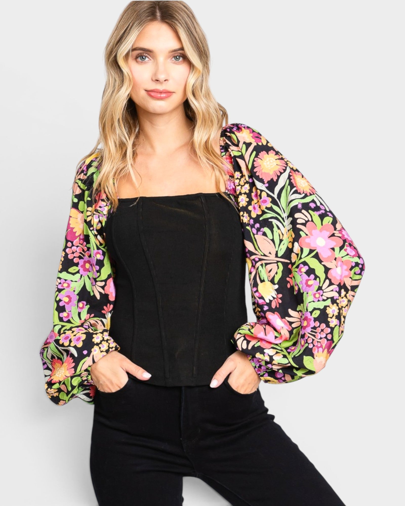 Woman wearing a black top and colorful floral jacket against a white background