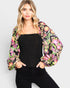 Woman wearing a black top and colorful floral jacket against a white background