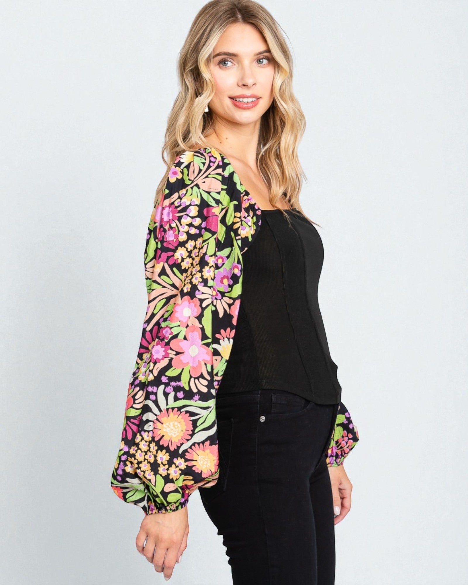 Woman wearing a colorful floral blouse over a black top on a light gray background