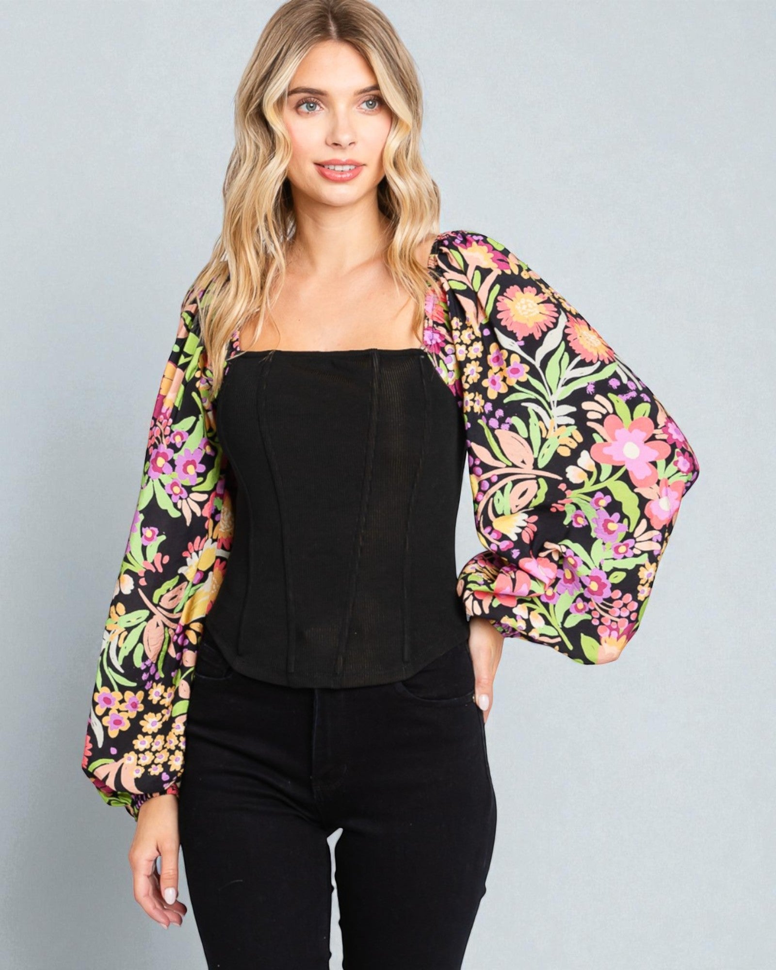 Woman wearing a black top and colorful floral jacket on a gray background