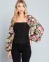 Woman wearing a black top and colorful floral jacket on a gray background