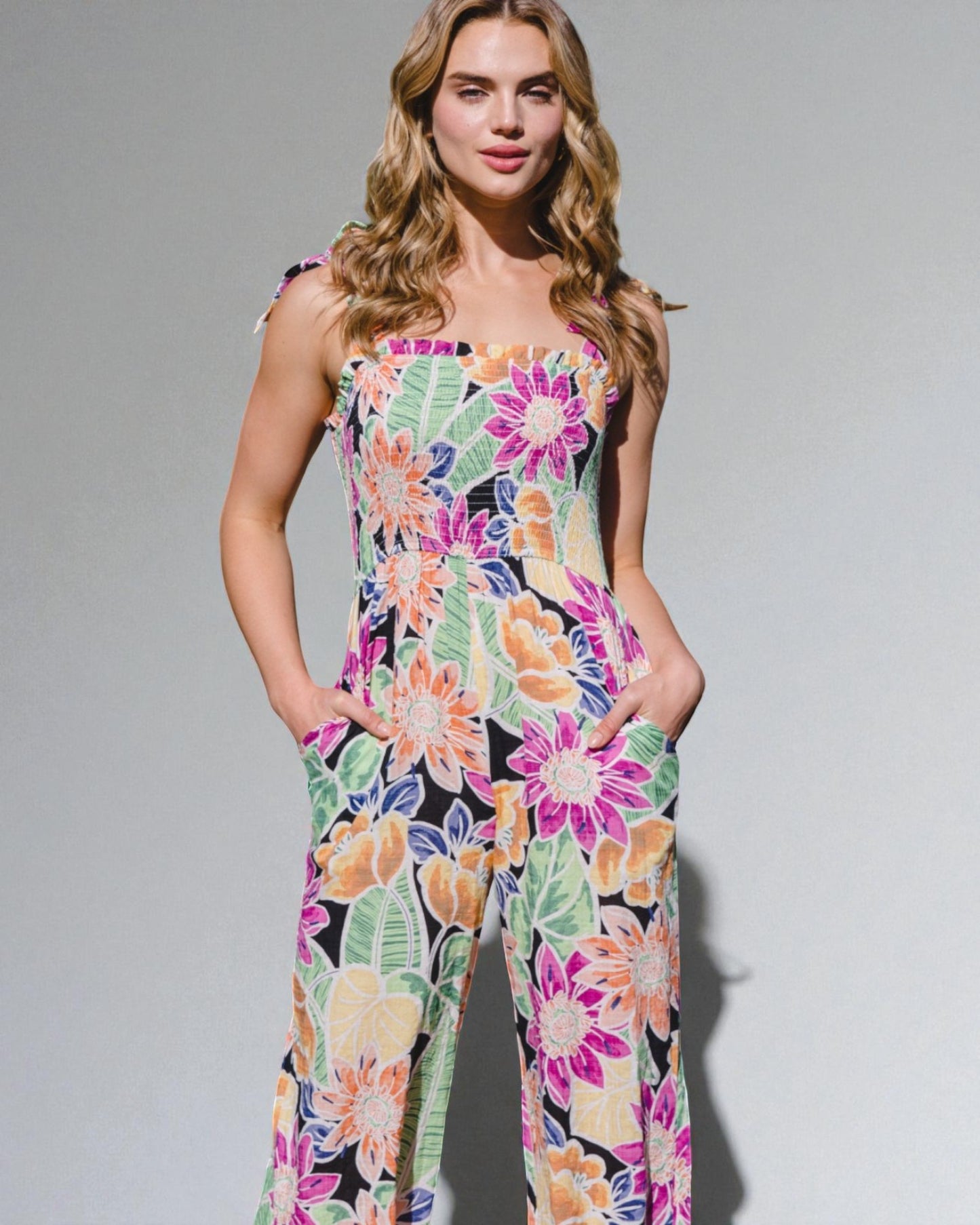 Woman wearing a colorful floral jumpsuit against a plain background