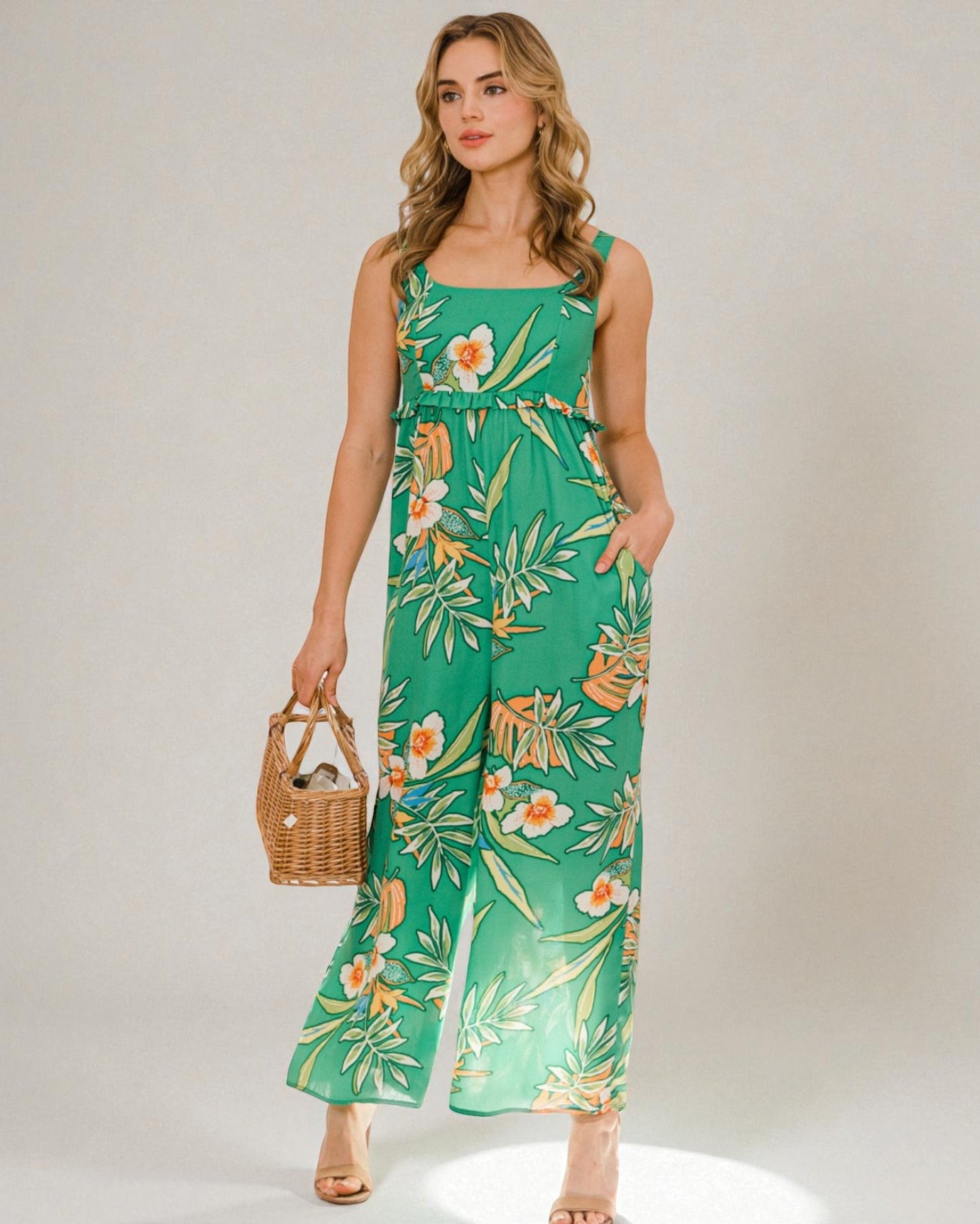 Woman wearing a green floral jumpsuit holding a woven bag against a plain background