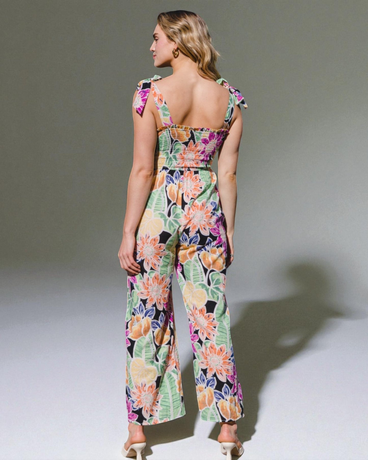 Woman wearing a colorful floral jumpsuit against a plain background