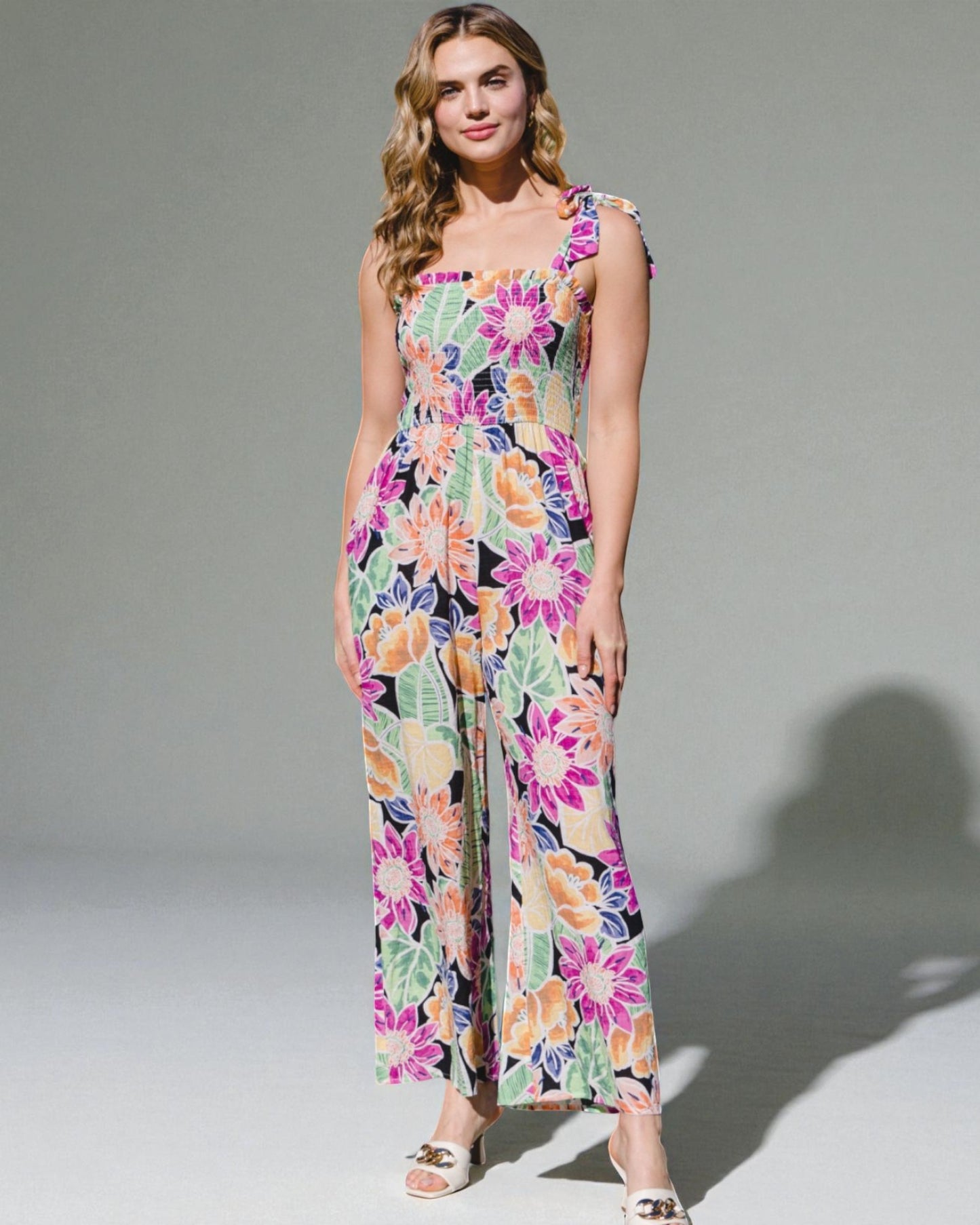 Woman wearing a colorful floral jumpsuit on a plain background