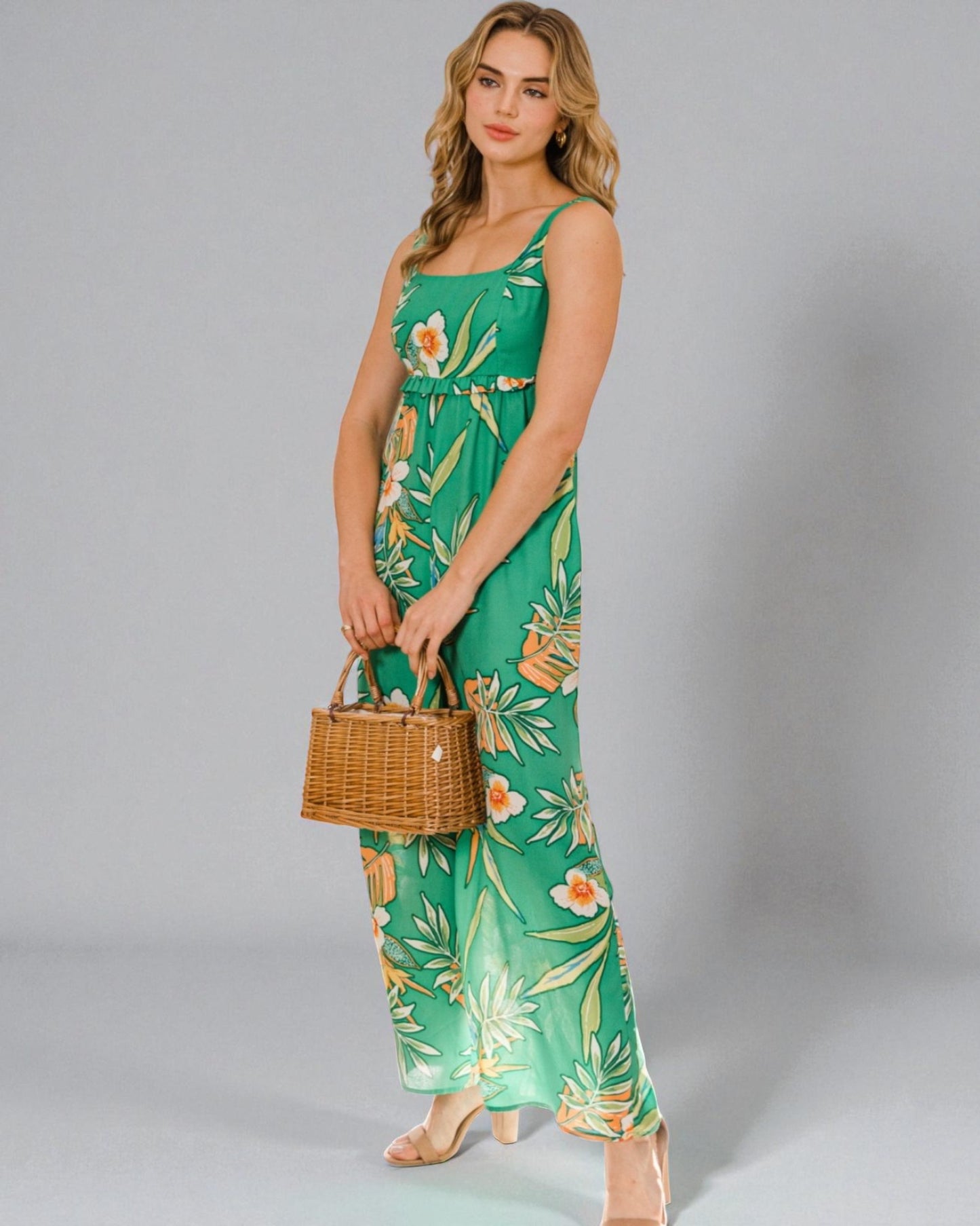 Woman wearing a green floral dress holding a woven bag on a gray background