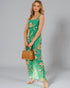 Woman wearing a green floral dress holding a woven bag on a gray background