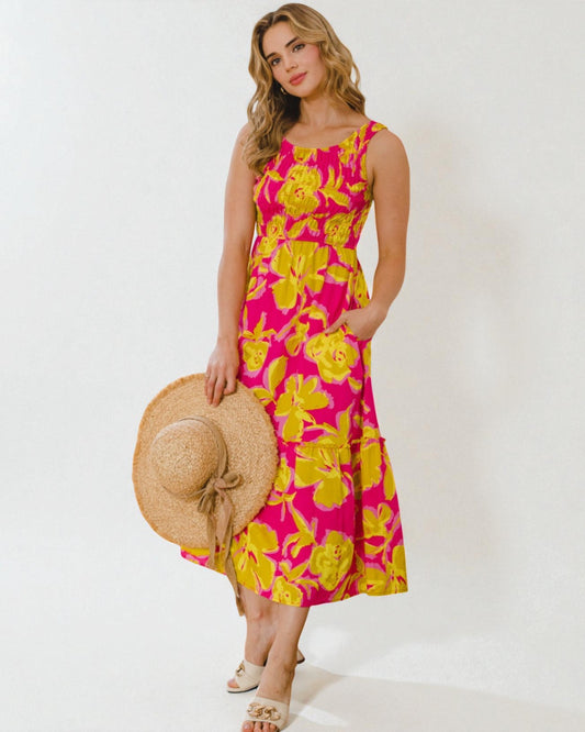Woman wearing a pink and yellow floral dress holding a straw hat on a white background