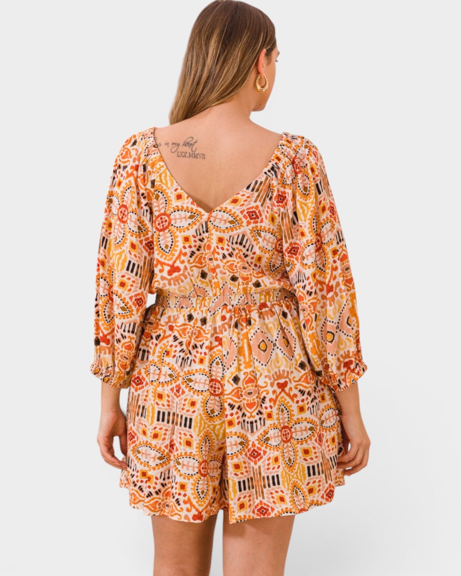 Woman wearing a patterned orange and yellow romper on a white background