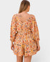 Woman wearing a patterned orange and yellow romper on a white background