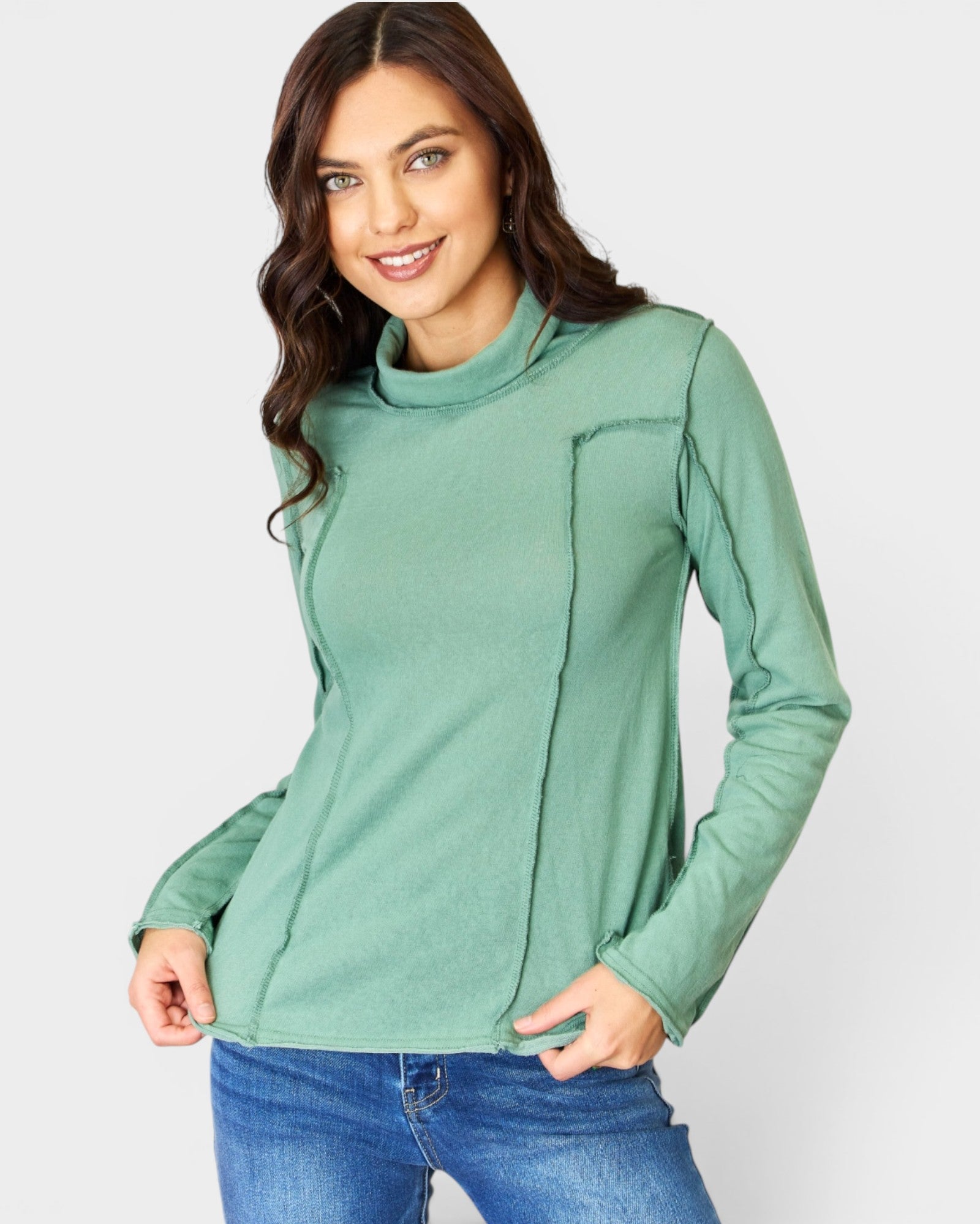 Woman wearing a green long-sleeve top with a cowl neck on a light gray background