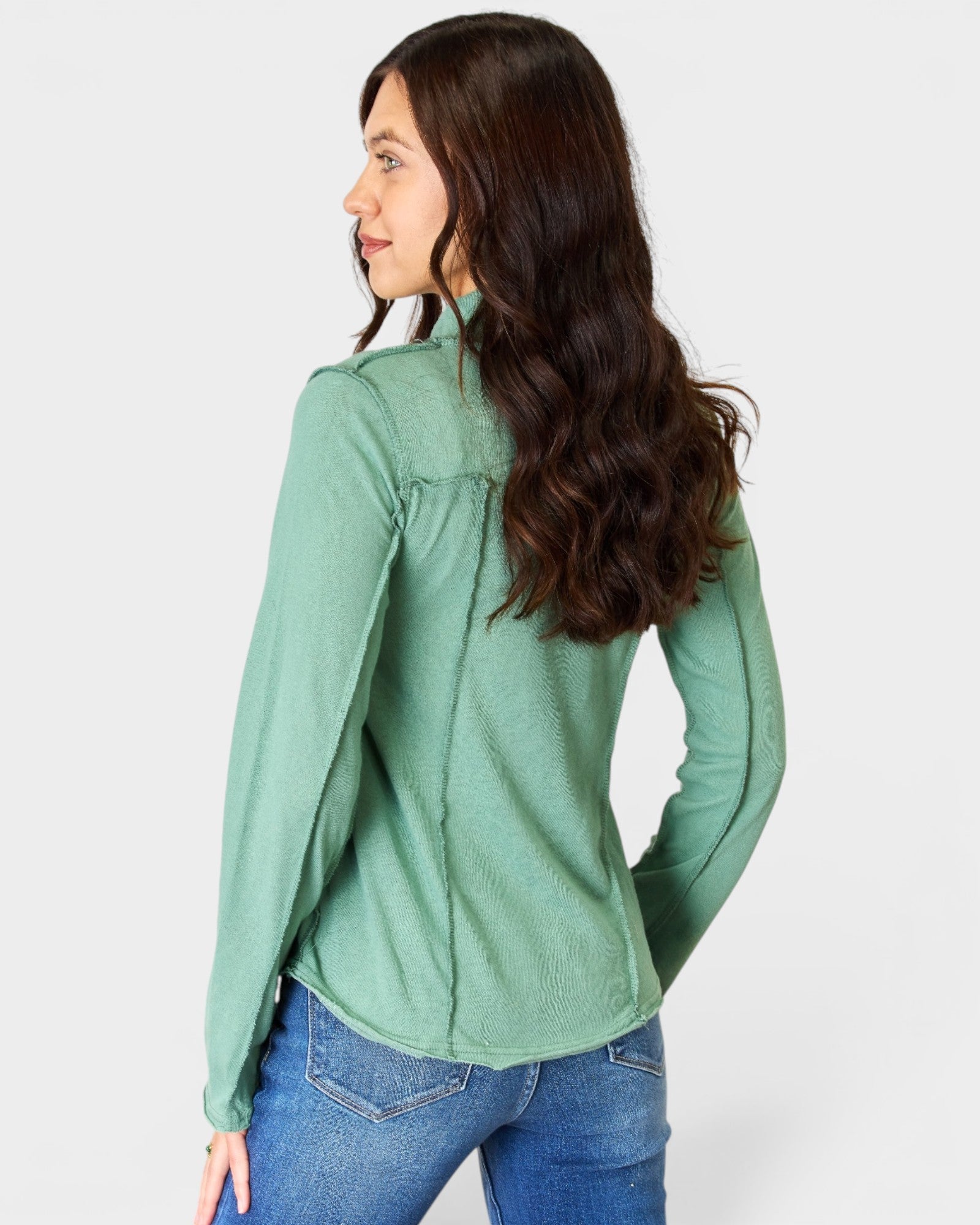 Woman wearing a green long-sleeve shirt and blue jeans on a white background