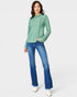 Woman wearing a green long-sleeve top and blue jeans on a white background