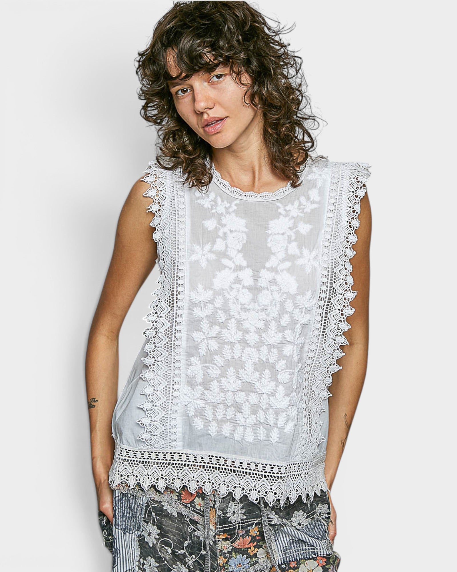 Woman wearing a sleeveless top with lace details on a plain background
